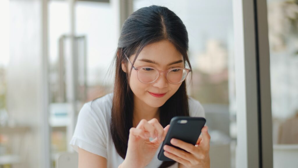 Freelance Asian women using mobile phone at a coffee shop.